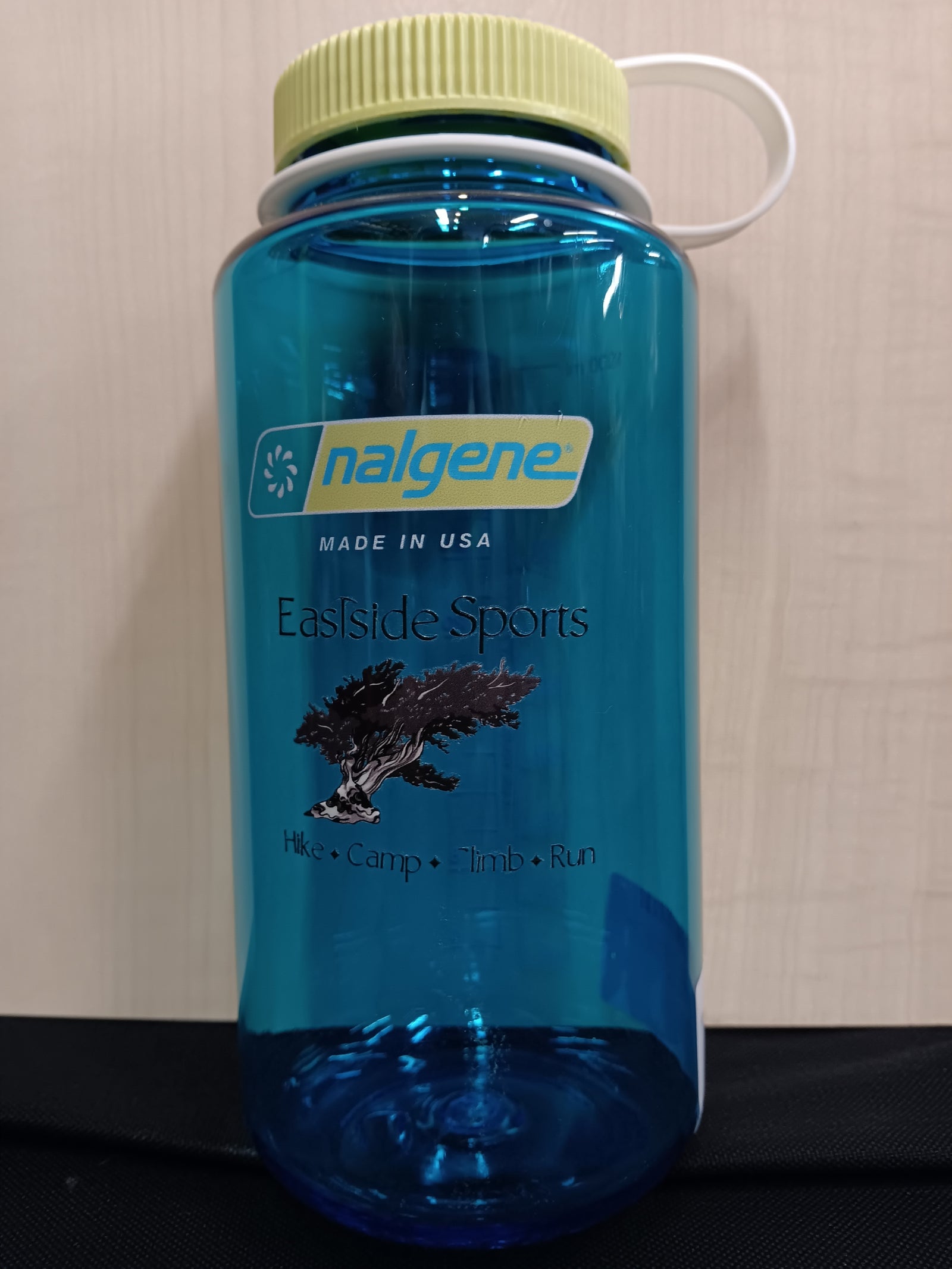 A translucent blue Nalgene water bottle with a light yellow cap and white carrying loop, featuring 'Eastside Sports' branding on the front, set against a neutral beige background.