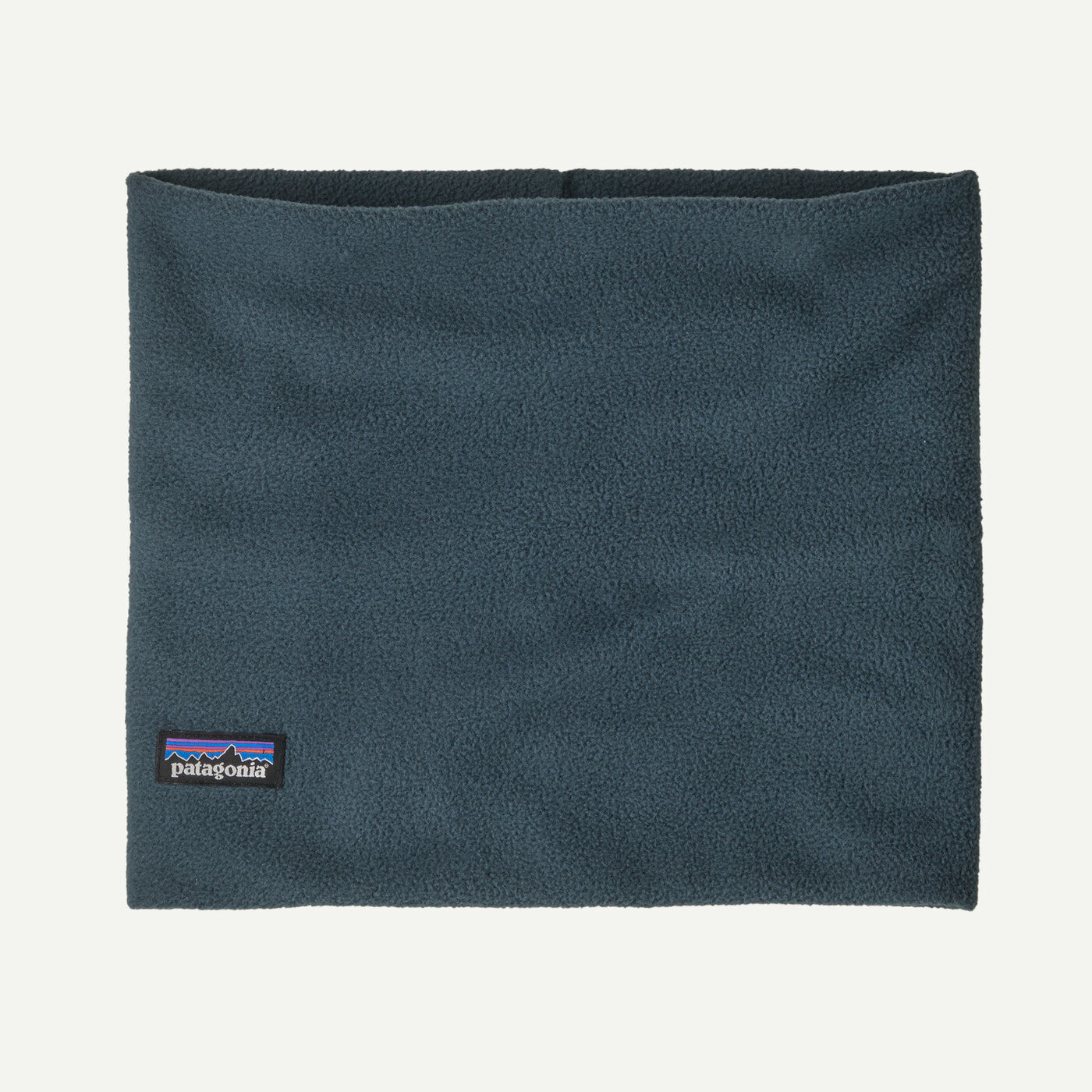 A dark slate blue fleece neck warmer with a small Patagonia logo patch on the bottom left, shown flat against a light off-white background.