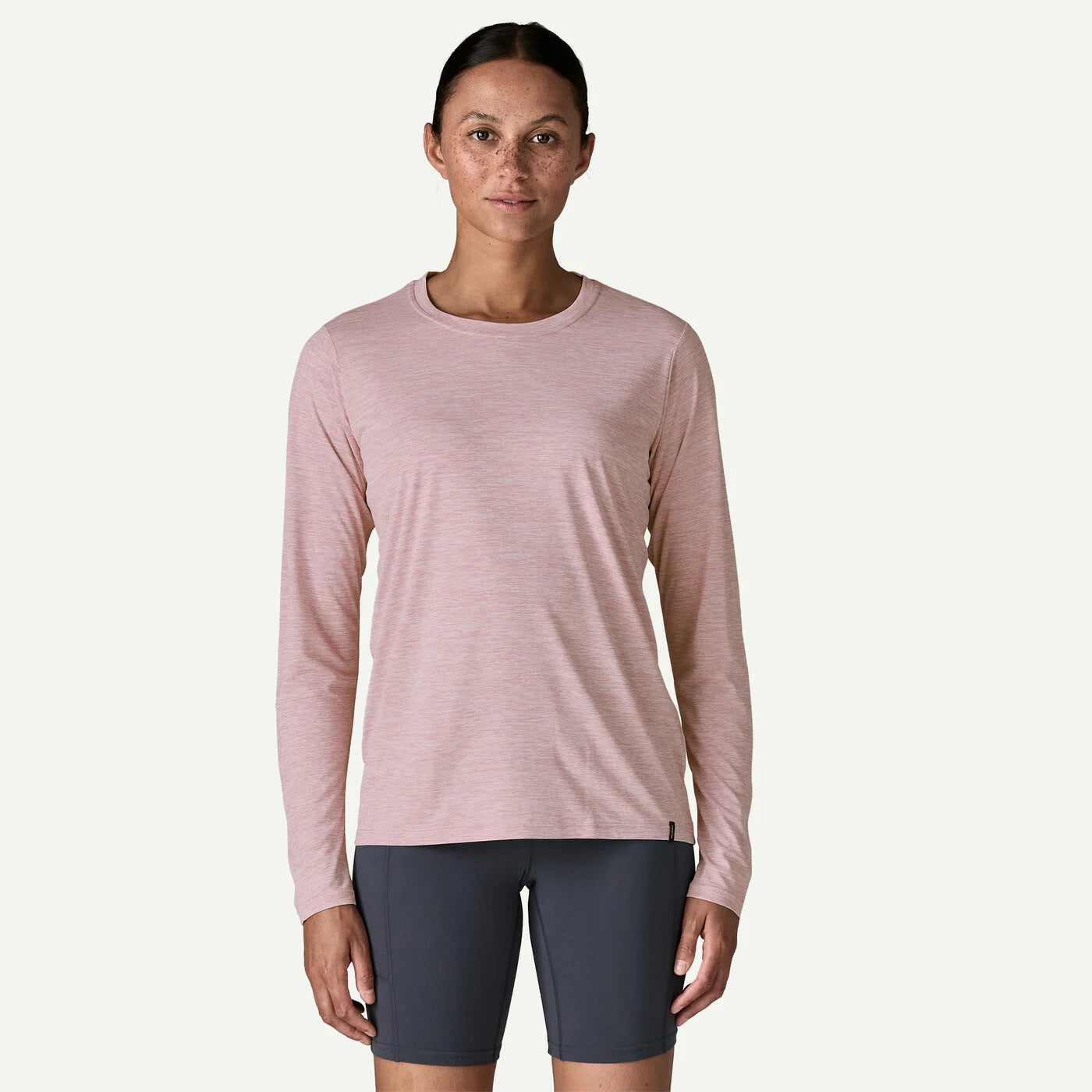Woman wearing a pink long-sleeve athletic shirt and dark shorts on a white background