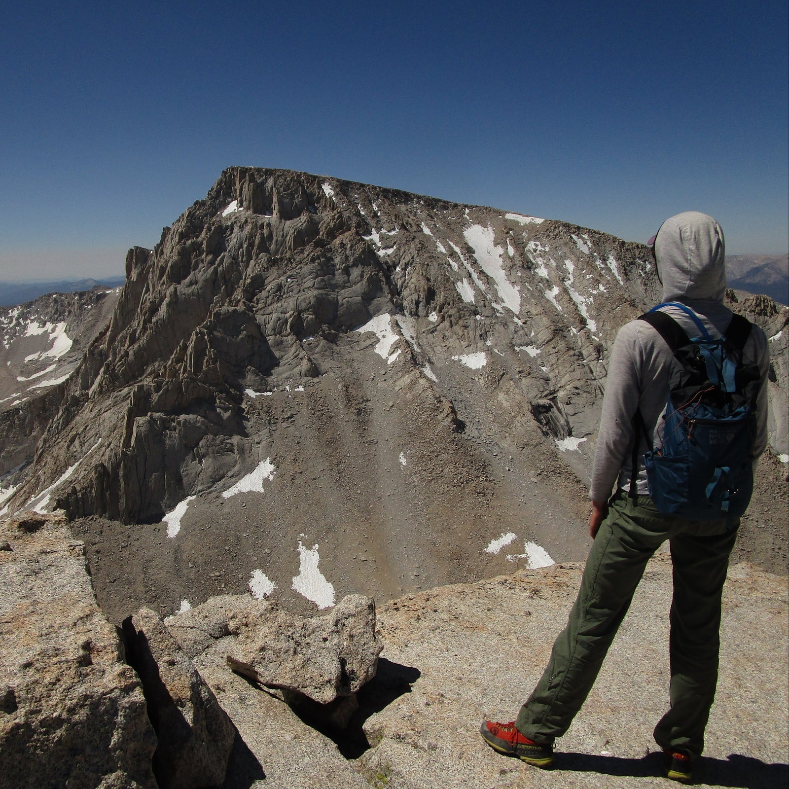 Person standing on a mountain peak looking at snow-capped mountains