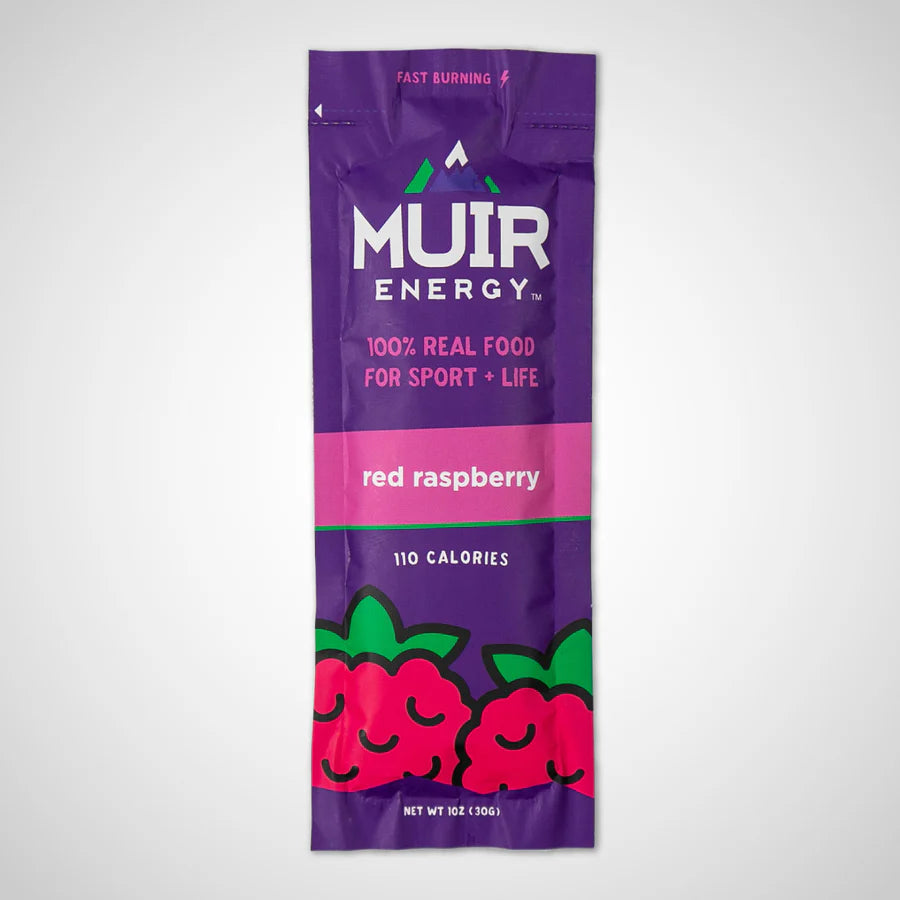 A single Muir Energy red raspberry flavored stick pack on a light gray background. The packaging is primarily purple with a pink band, white text, and a cartoon raspberry illustration at the bottom.