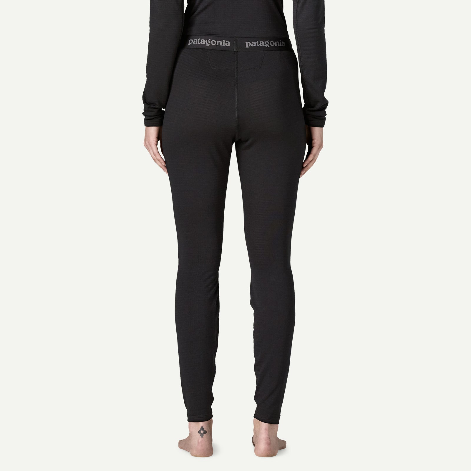 Rear view of a person wearing black Patagonia full-length leggings and a black long-sleeve top against a plain off-white background.