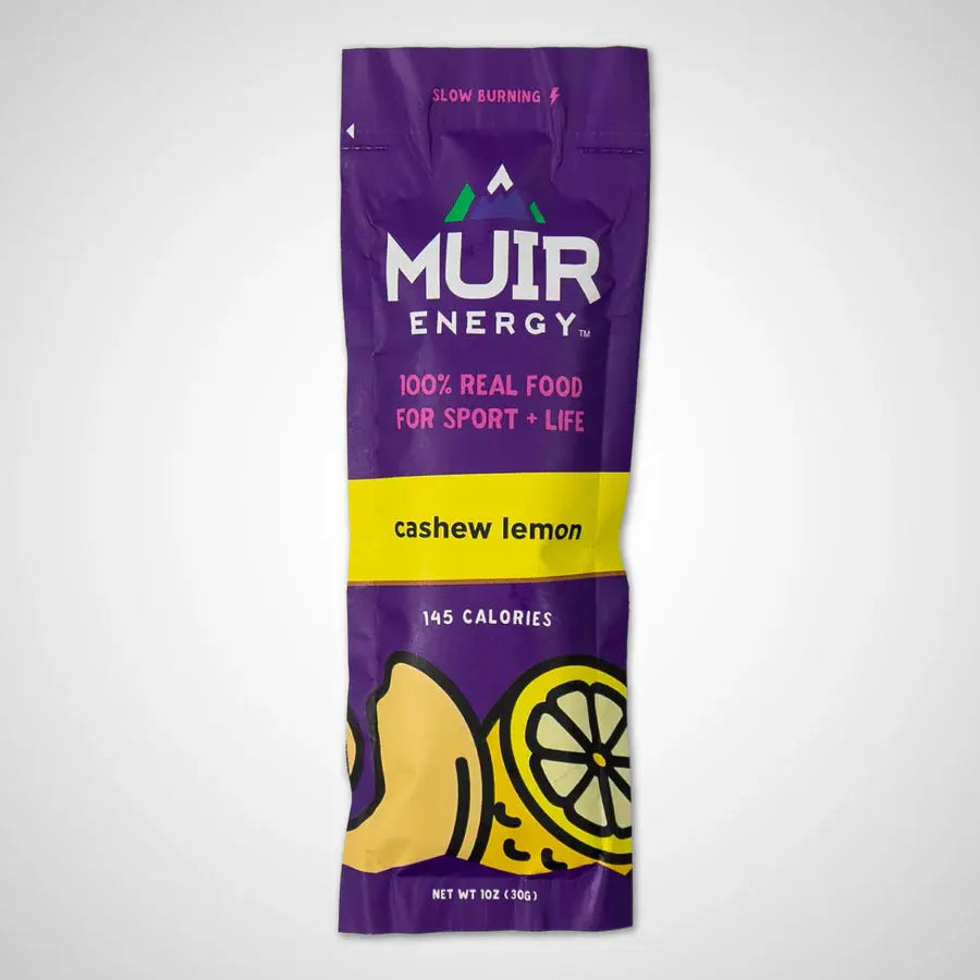 A single Muir Energy slow-burning food packet in the cashew lemon flavor, featuring a purple and yellow design with illustrations of a cashew and a lemon slice.