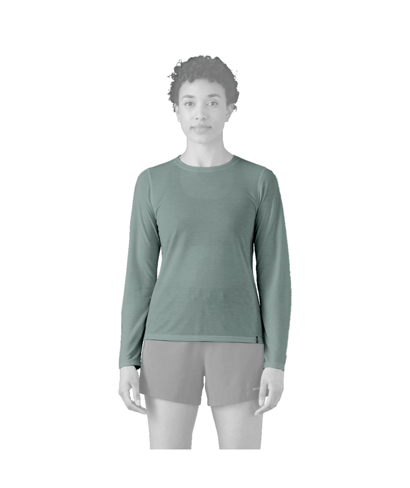 A grayscale model wearing a sage green long-sleeve athletic top and light gray shorts, standing against a solid green background.