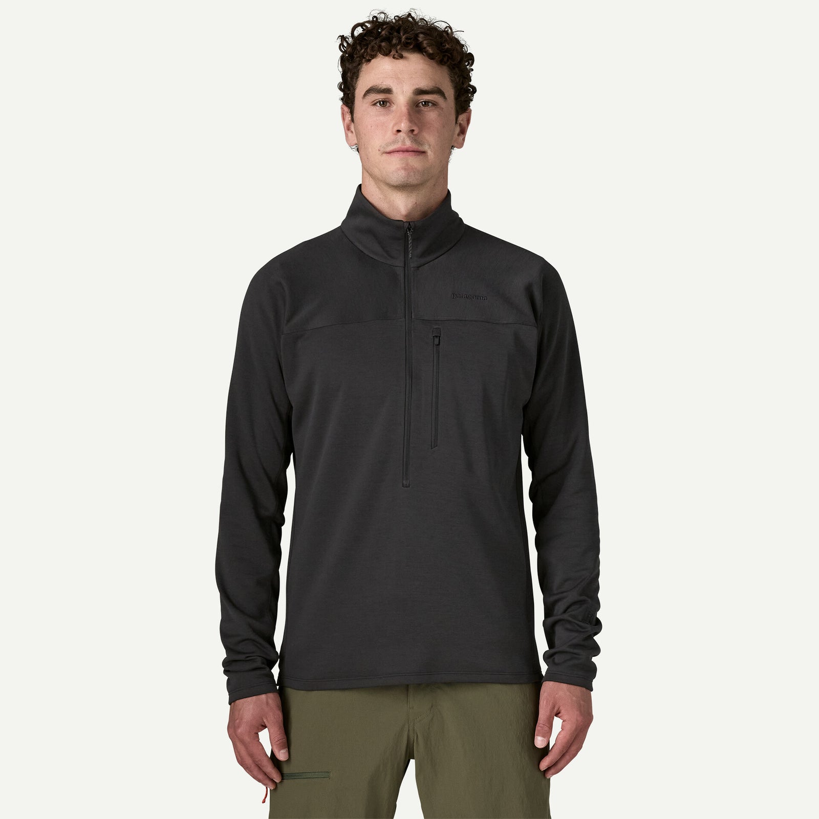 A man wearing a dark gray quarter-zip fleece pullover and olive green pants, standing against a light gray background.