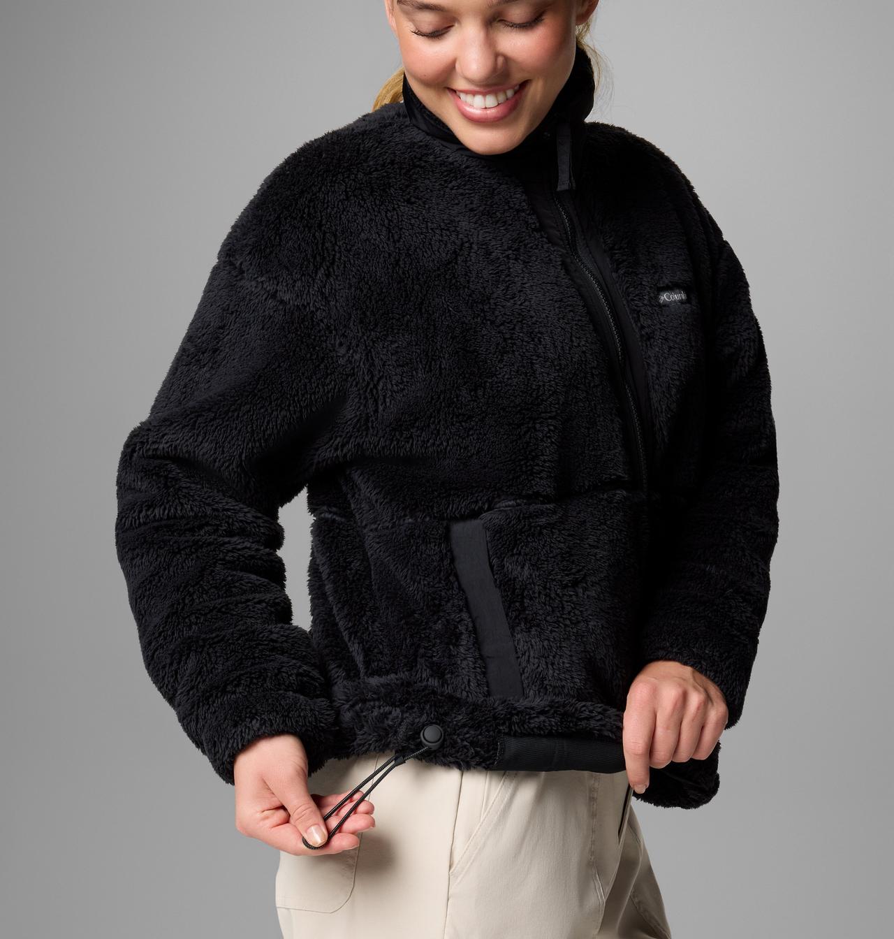 Person wearing a black fleece jacket on a gray background, detail of drawcord in bottom hem
