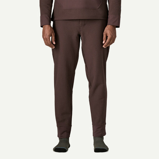 A person wearing textured brown pants and a matching brown top, standing against a plain off-white background.