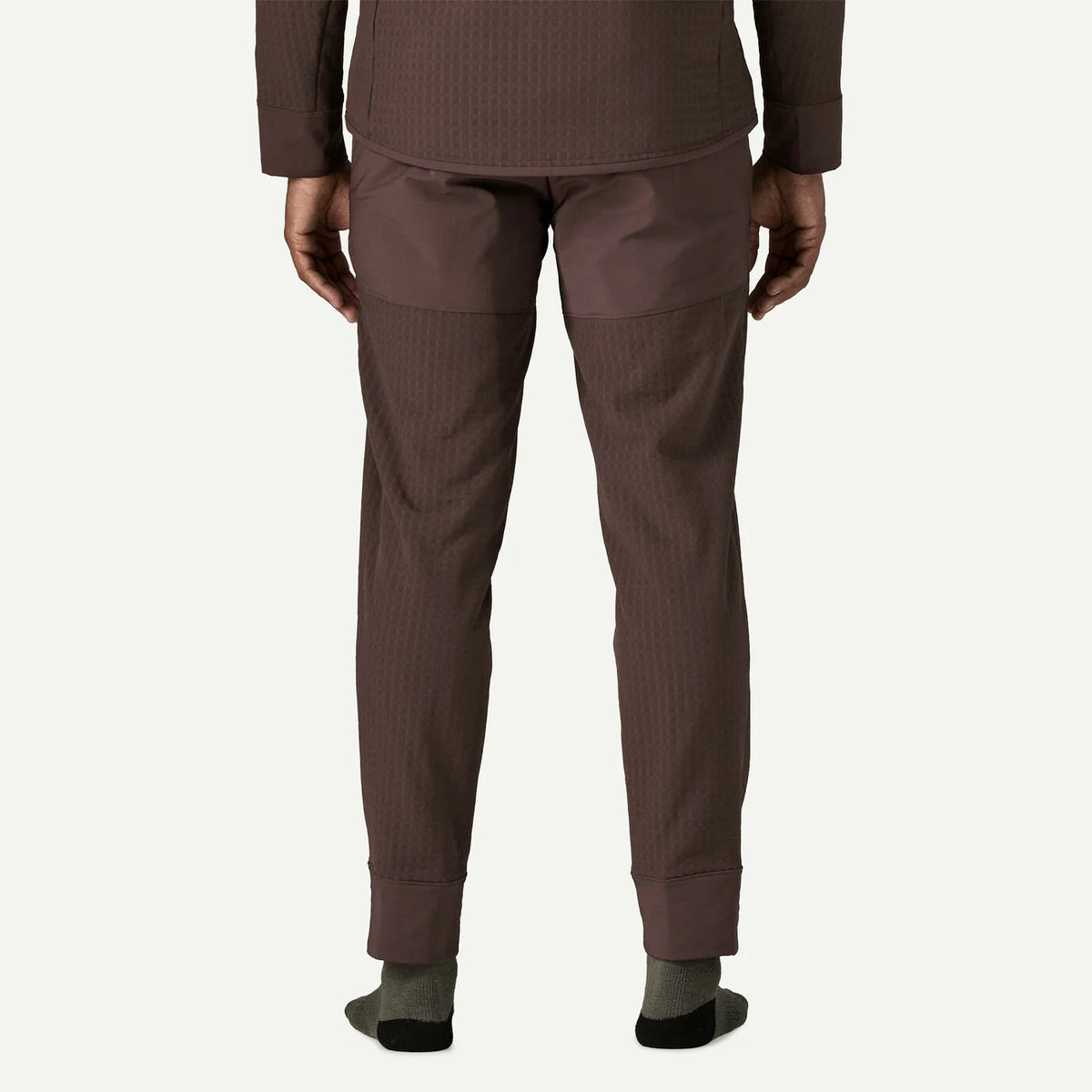 Rear view of a person wearing brown textured pants with a matching long-sleeve top, standing against a light off-white background.