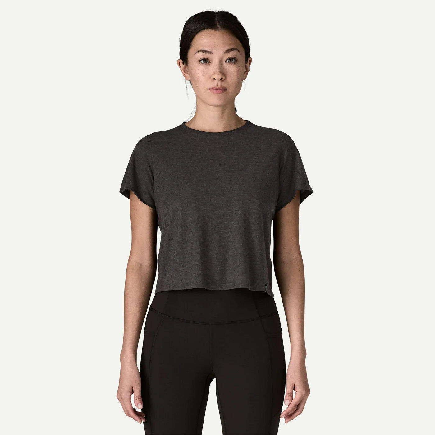 Woman wearing a dark gray t-shirt and black leggings on a white background