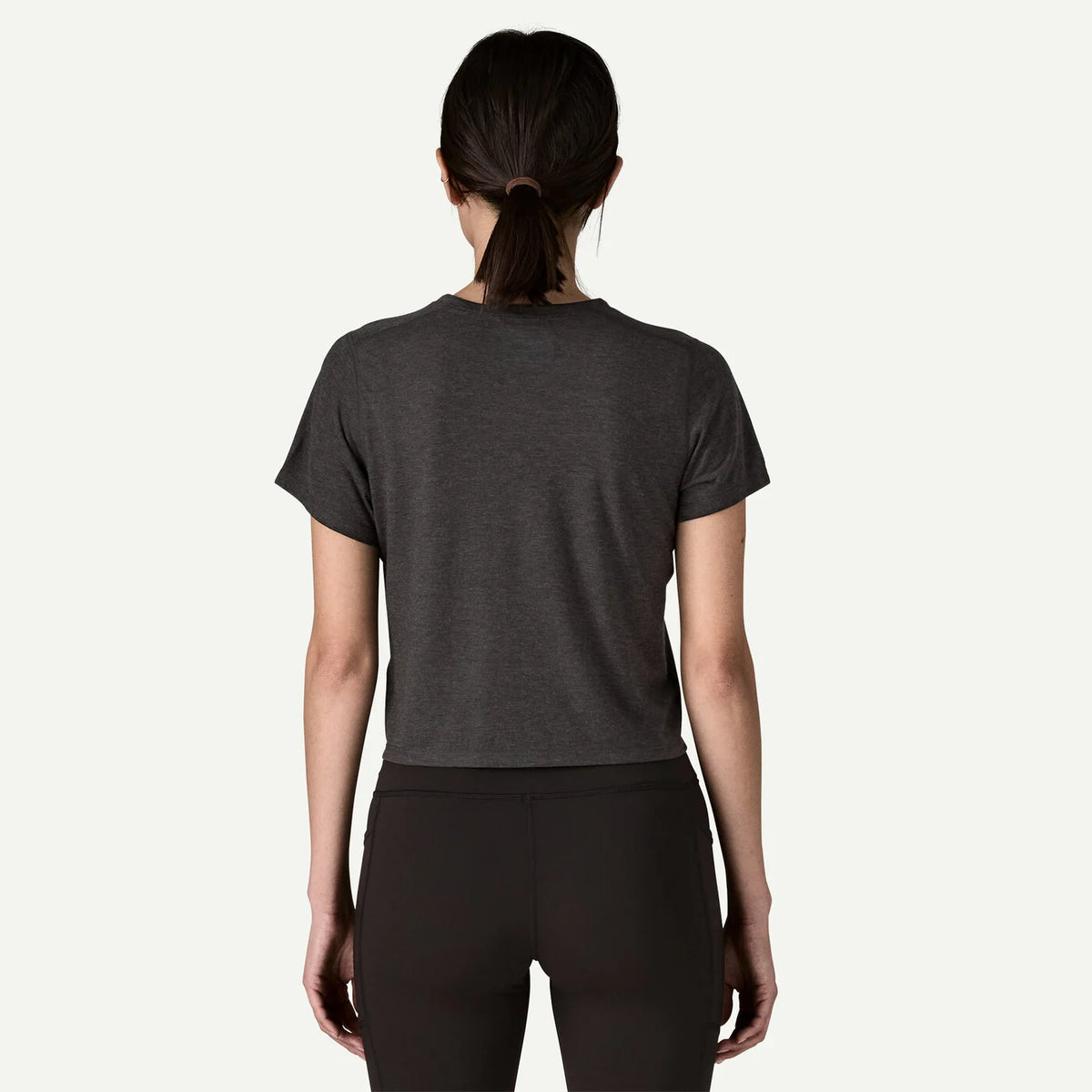 Person wearing a dark gray t-shirt and black leggings on a white background