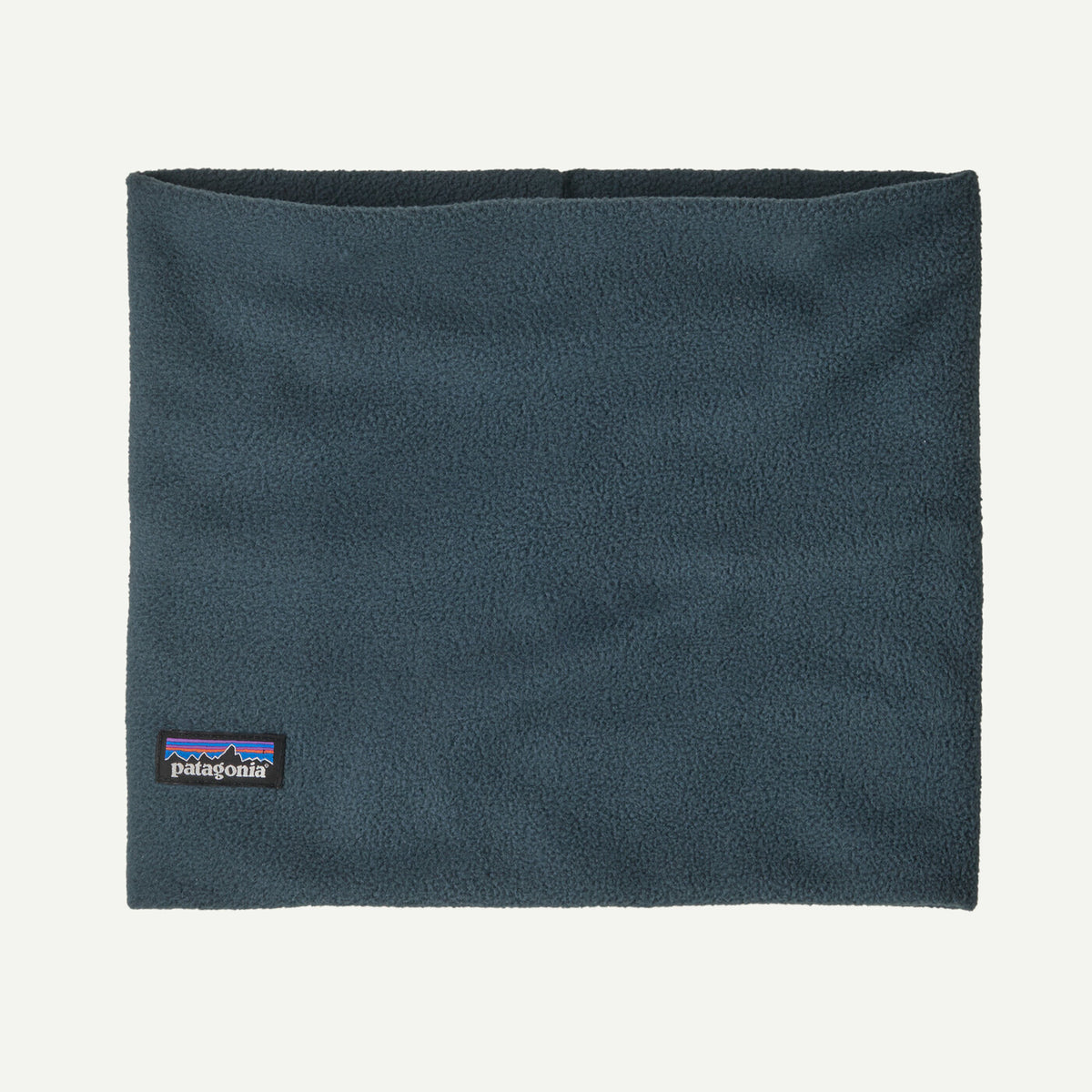 A dark slate blue fleece neck warmer with a small Patagonia logo patch on the bottom left, shown flat against a light off-white background.