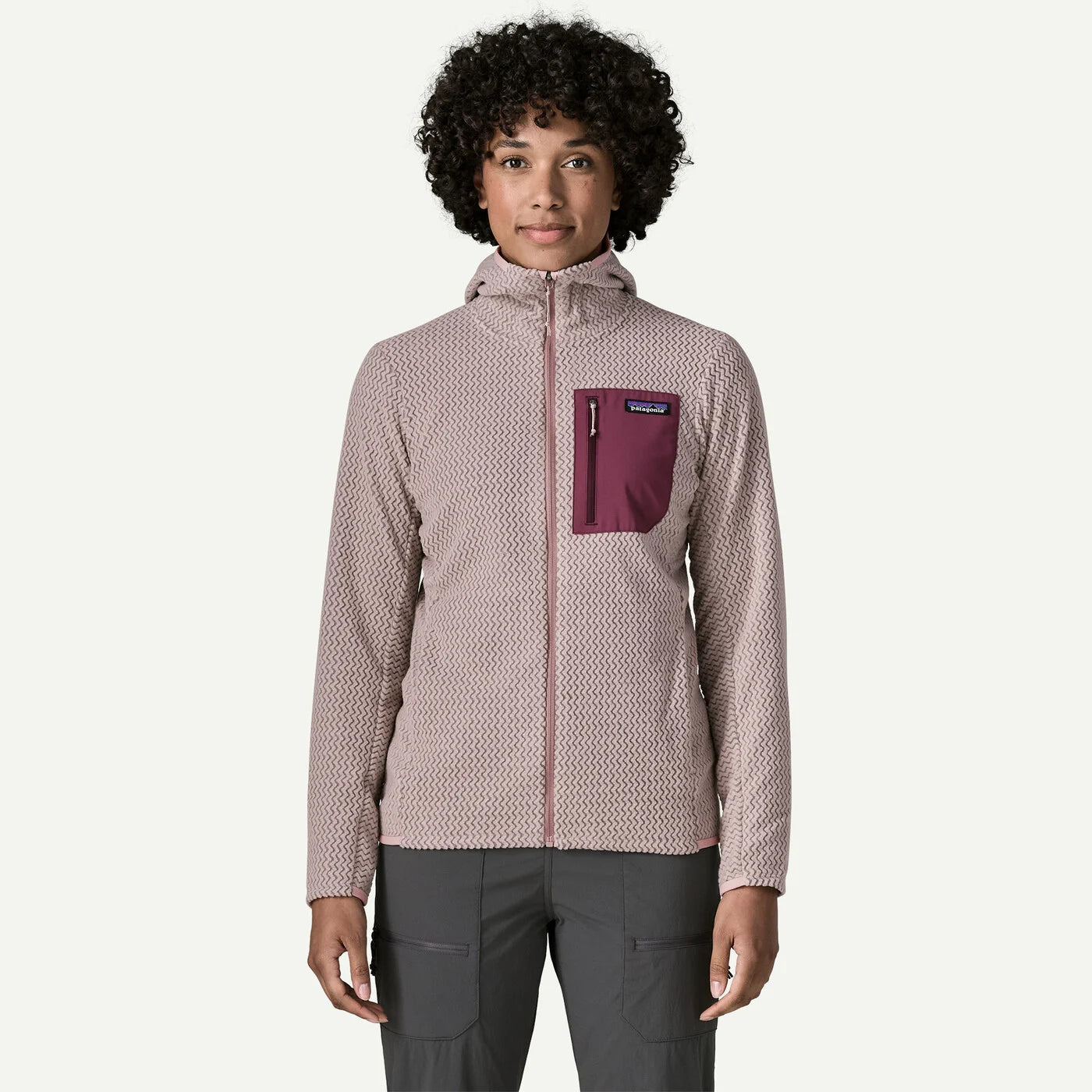 A woman modeling a Patagonia fleece jacket with a textured pattern in dusty pink and white, featuring a solid burgundy chest pocket with a Patagonia logo.