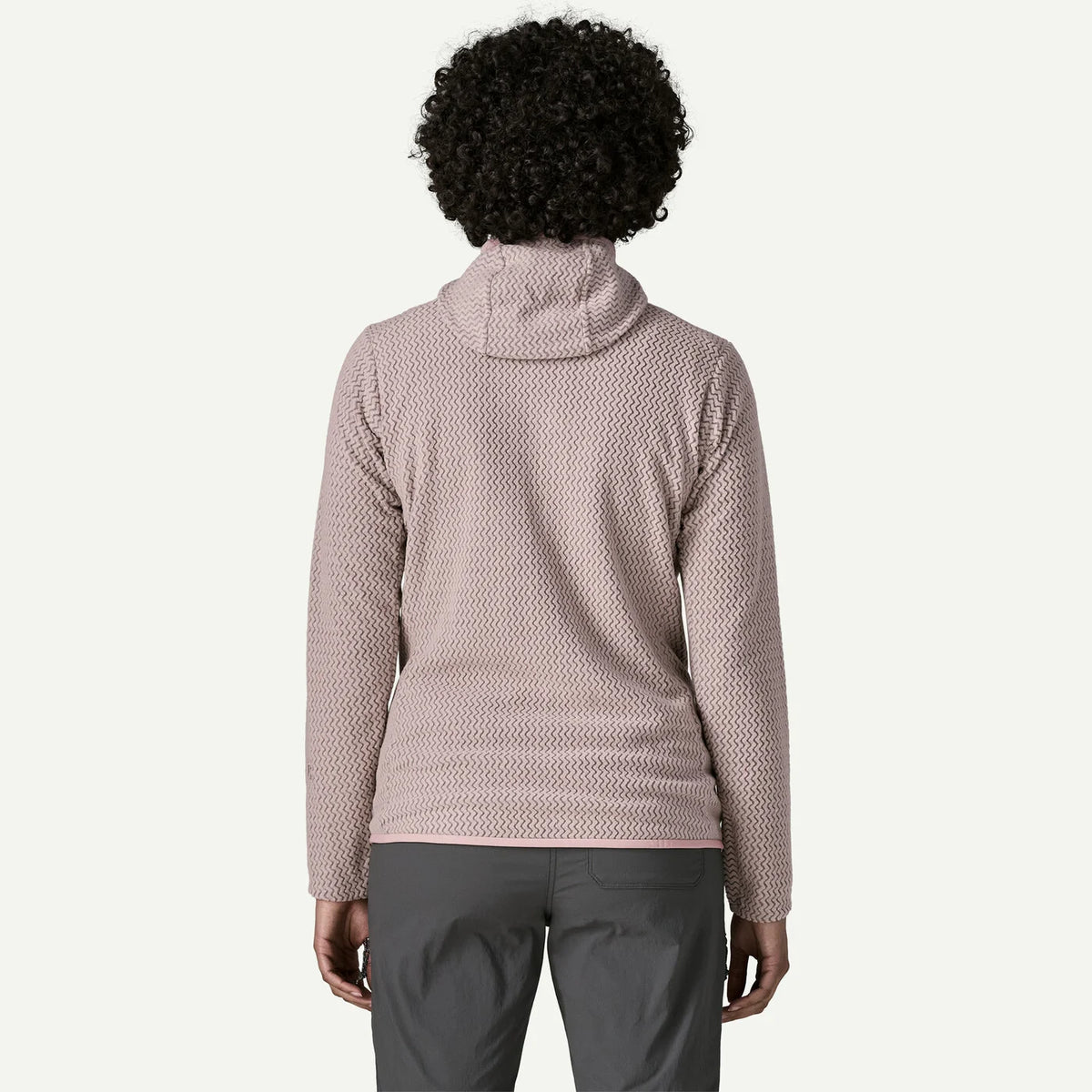 A person shown from the back wearing a textured, waffle-knit pullover top in a dusty rose pink color, paired with dark gray pants, against a plain off-white background.