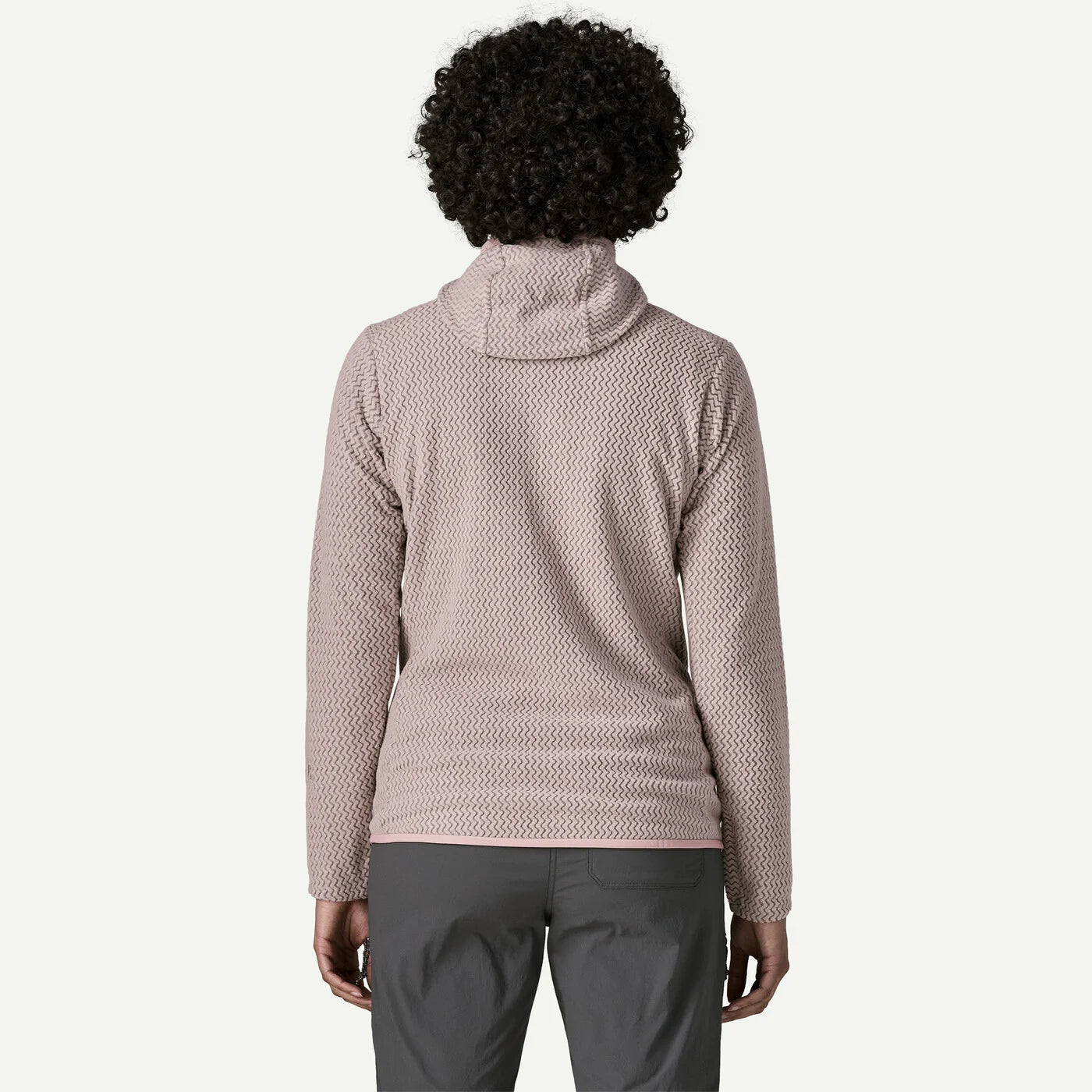 A person shown from the back wearing a textured, waffle-knit pullover top in a dusty rose pink color, paired with dark gray pants, against a plain off-white background.