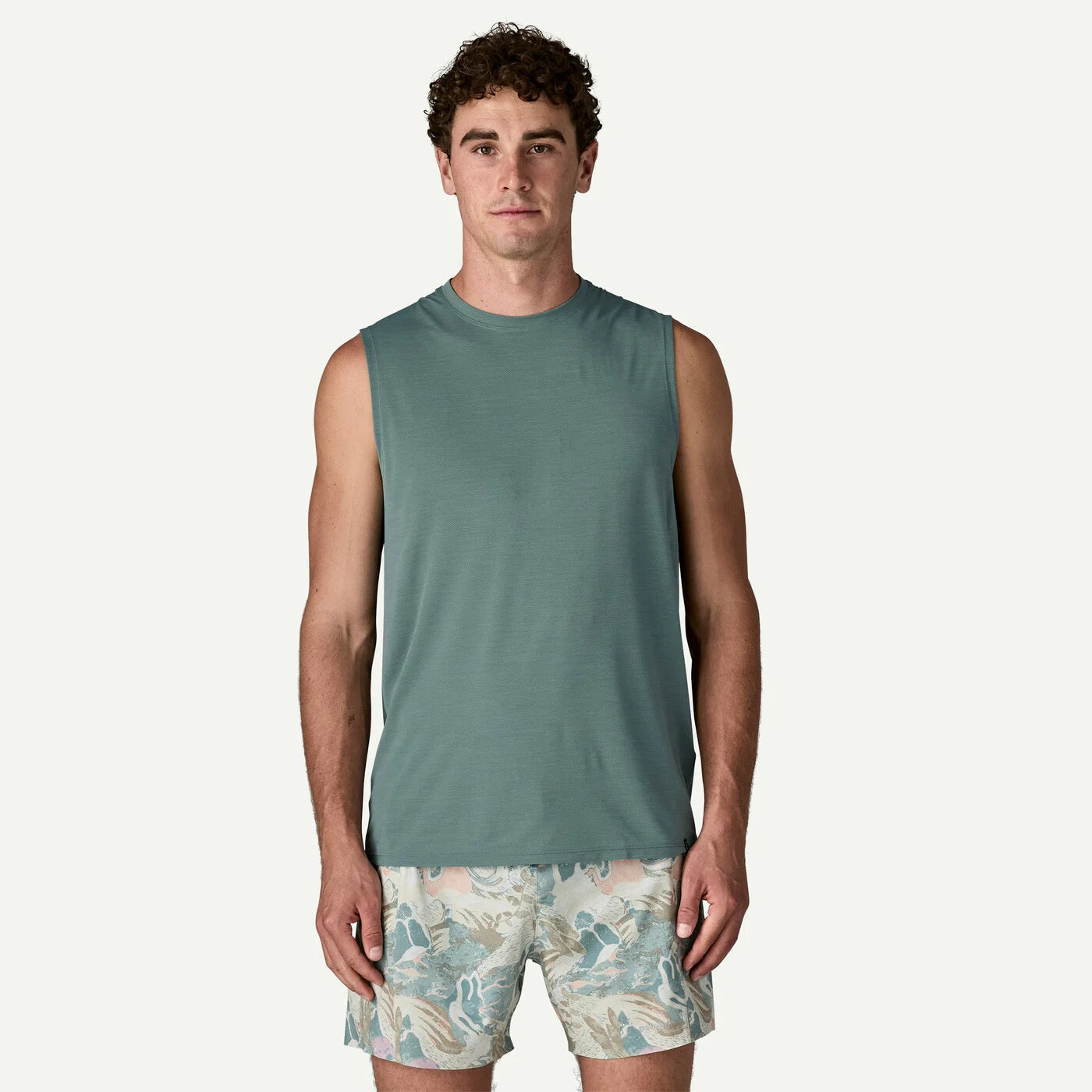 Man wearing a sleeveless sage colored shirt and patterned shorts on a white background