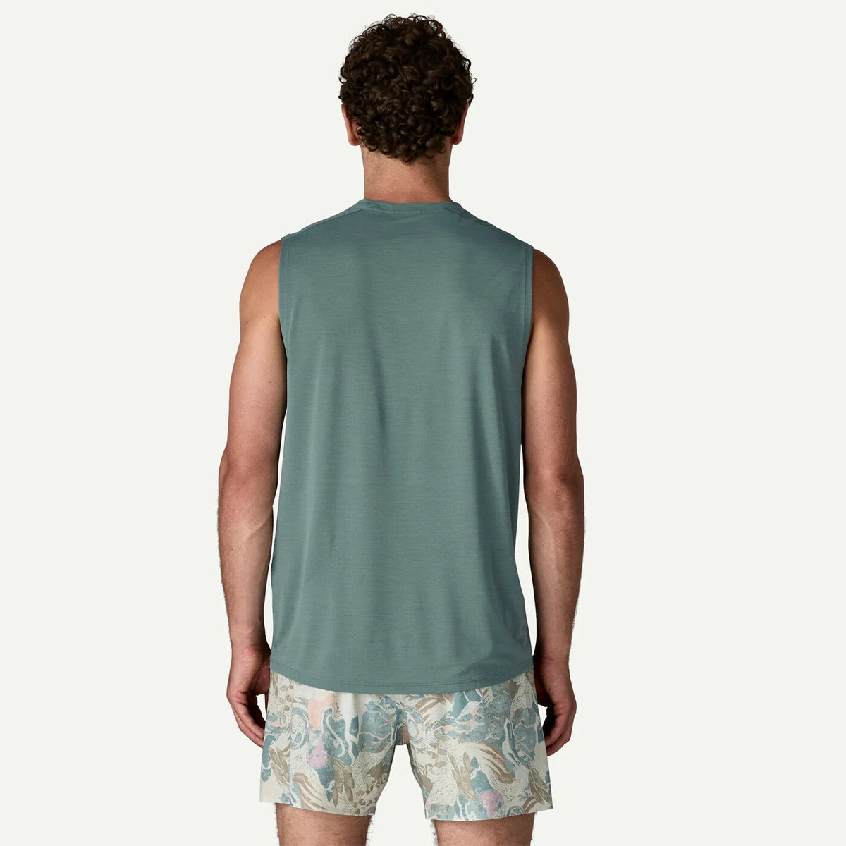 Man wearing a sleeveless sage colored shirt and patterned shorts on a white background