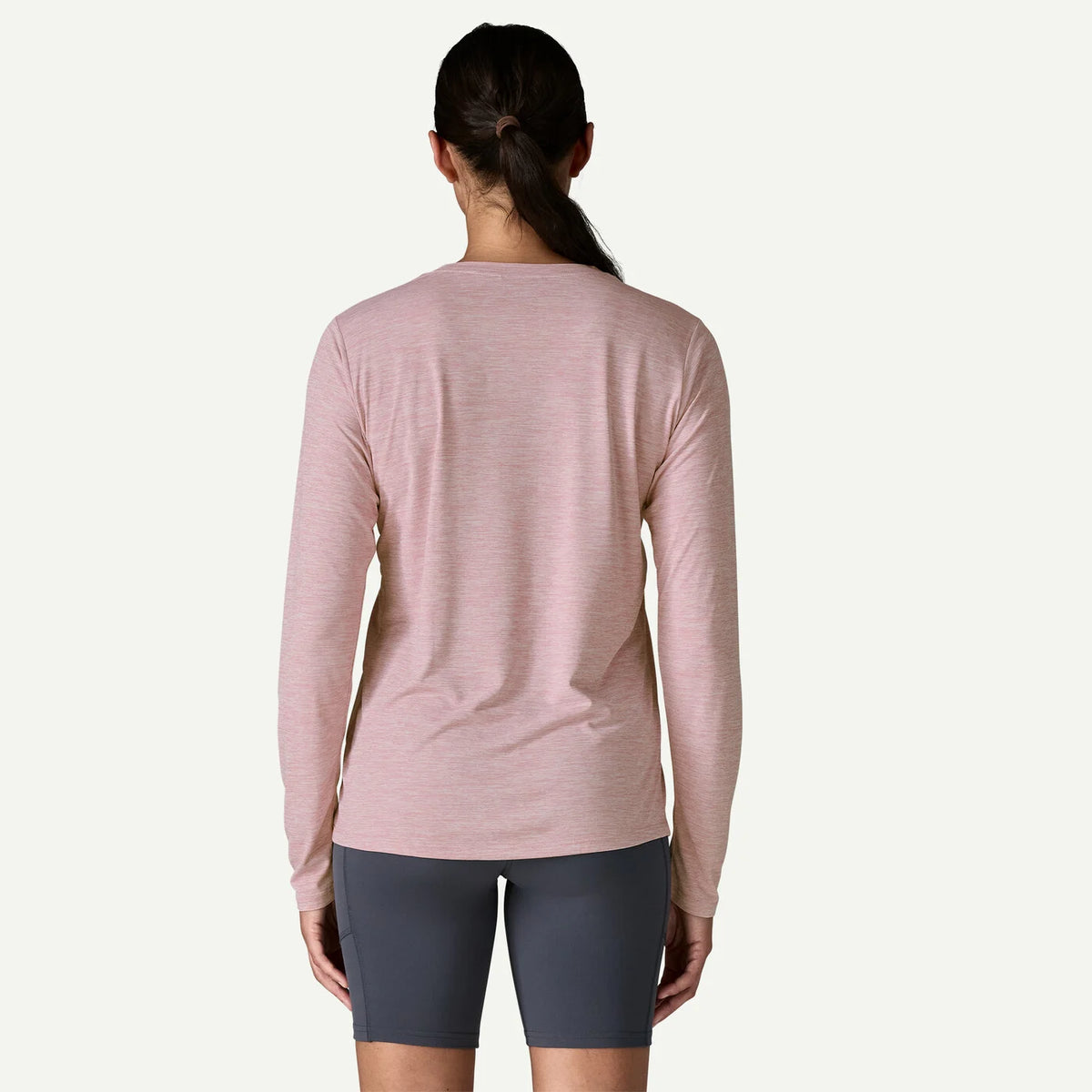 Person wearing a pink long-sleeve top and gray shorts on a white background