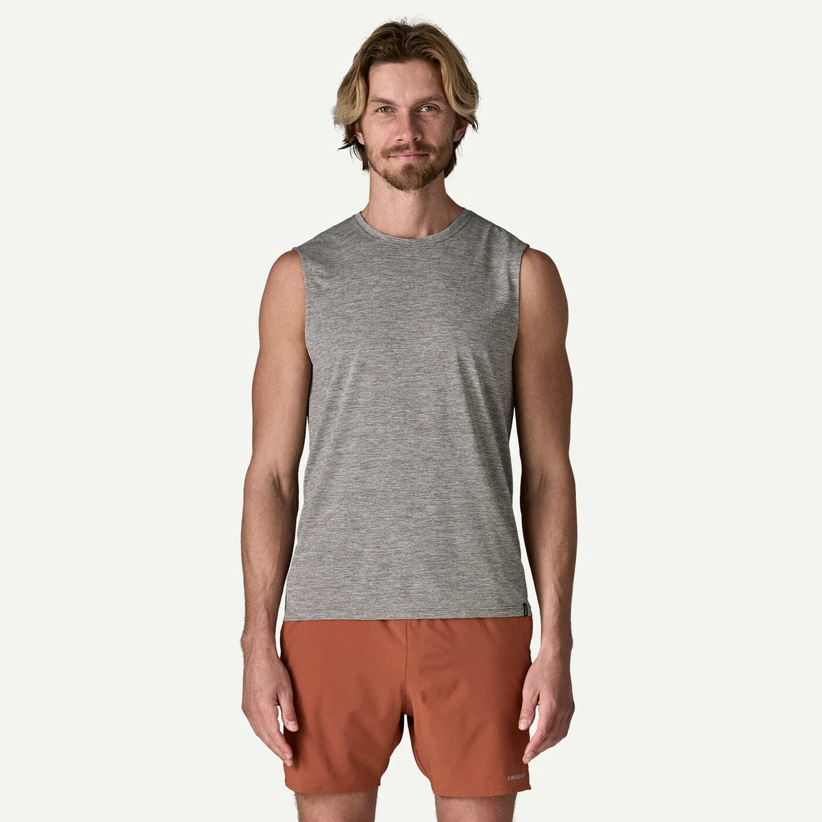 Man wearing a gray sleeveless shirt and brown shorts on a white background