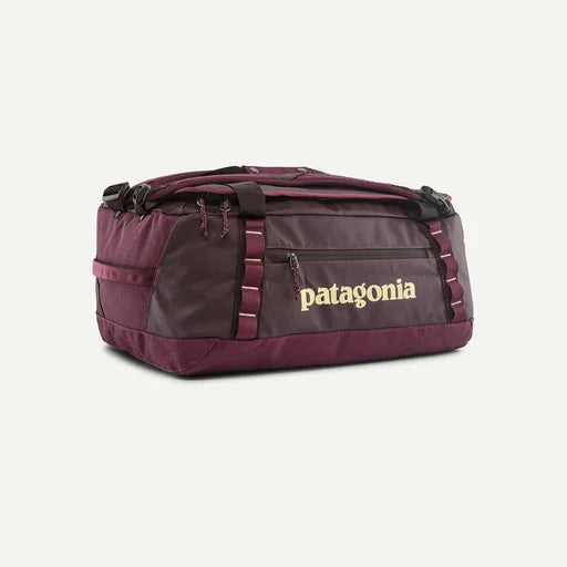 A Patagonia duffel bag in a deep burgundy color, featuring a front zippered pocket with the brand name printed in gold, set against a plain off-white background.