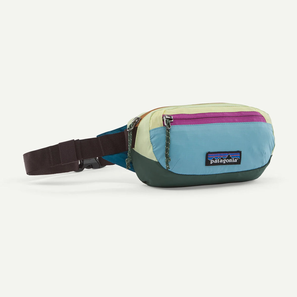 A Patagonia colorblock fanny pack with a light blue, cream, and dark green body, a purple zipper, and a dark brown adjustable strap, shown on a light gray background.