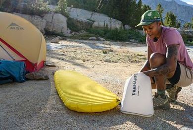 a photo of a model blowing up a thermarest neoair xlite nxt pad with the pump sack