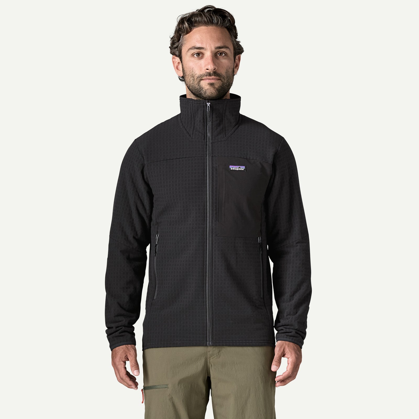 A man wearing a black Patagonia full-zip fleece jacket with a stand-up collar and zippered hand pockets, paired with khaki pants, against a plain white background.