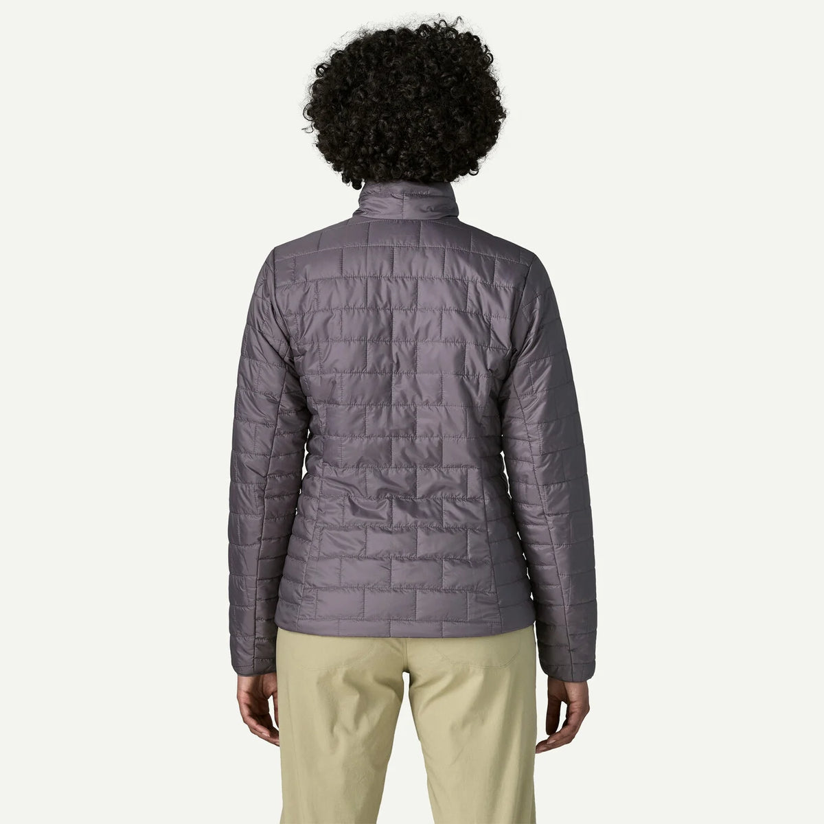 A person shown from the back wearing a quilted zip-front puffer jacket in a muted gray-purple tone, paired with light khaki pants, against a plain light background.