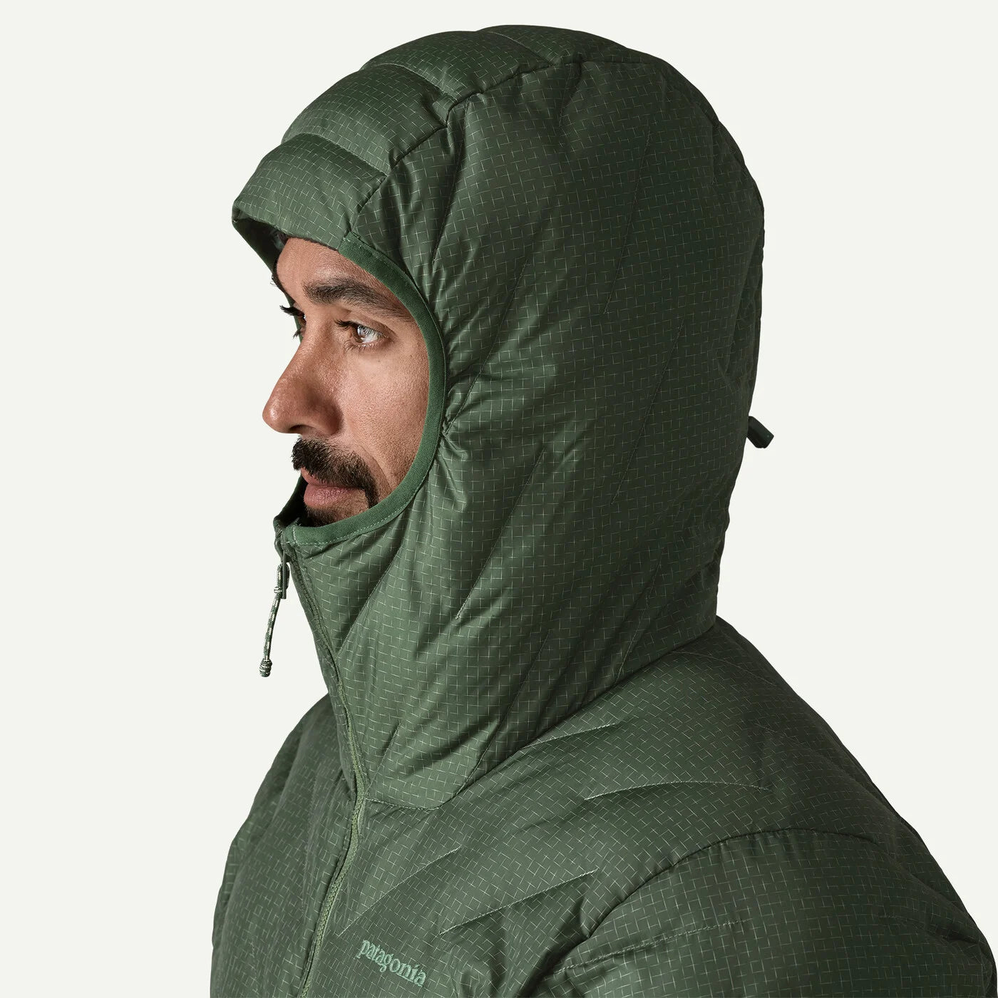 A man in profile wearing a Patagonia hooded jacket in a dark olive green color, shown against a plain white background.