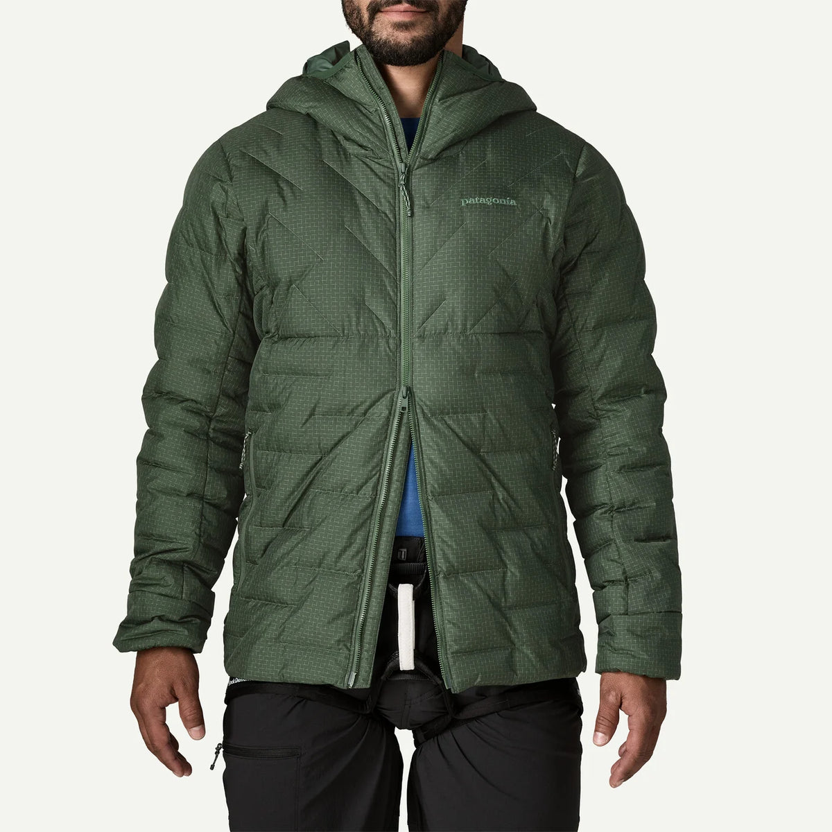 A man wearing a green hooded puffer jacket with a subtle grid texture, shown from the chin down against a light gray background.