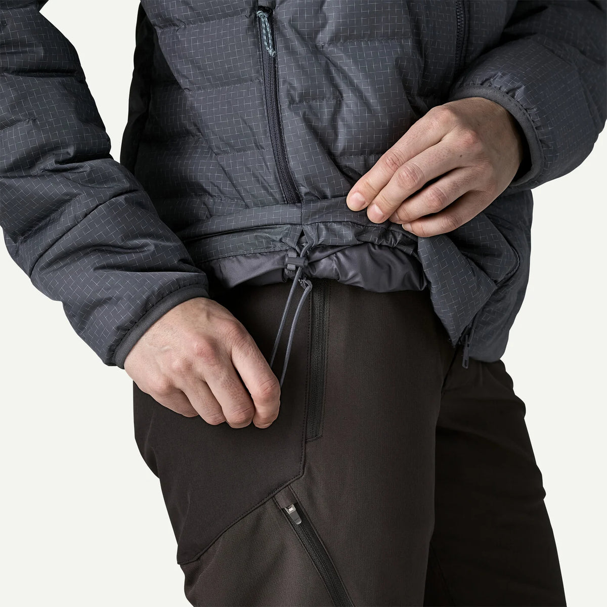 Close-up of a person wearing a dark gray quilted jacket and dark brown pants, adjusting the drawstring waist of the jacket.
