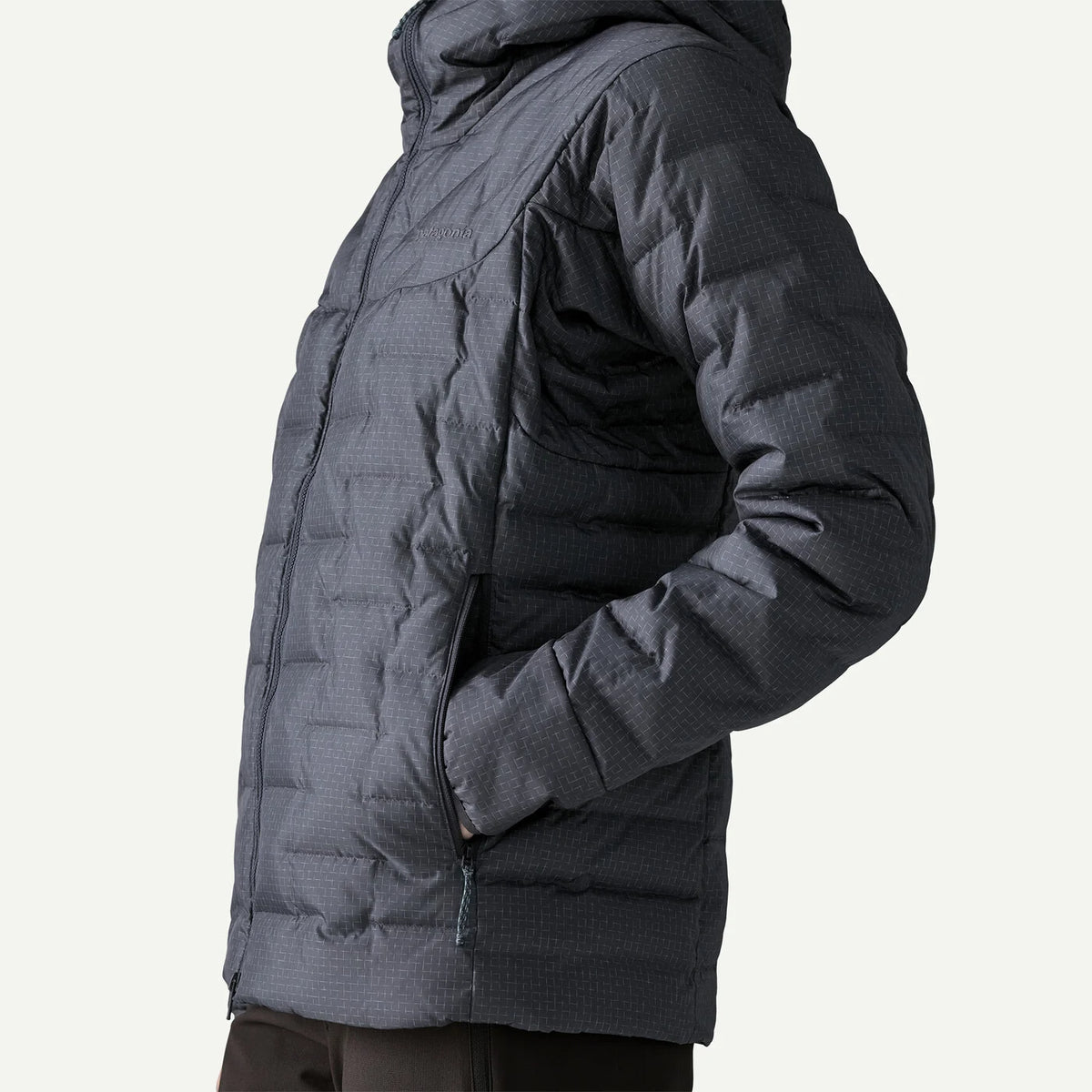 A close-up side view of a person wearing a dark gray hooded puffer jacket with a subtle grid texture, set against a plain off-white background.