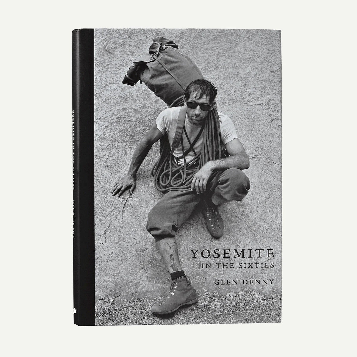 A hardcover book titled "Yosemite in the Sixties" by Glen Denny, featuring a black-and-white cover photograph of a man climbing in Yosemite with a backpack and rope. The book is photographed upright against a plain light background.