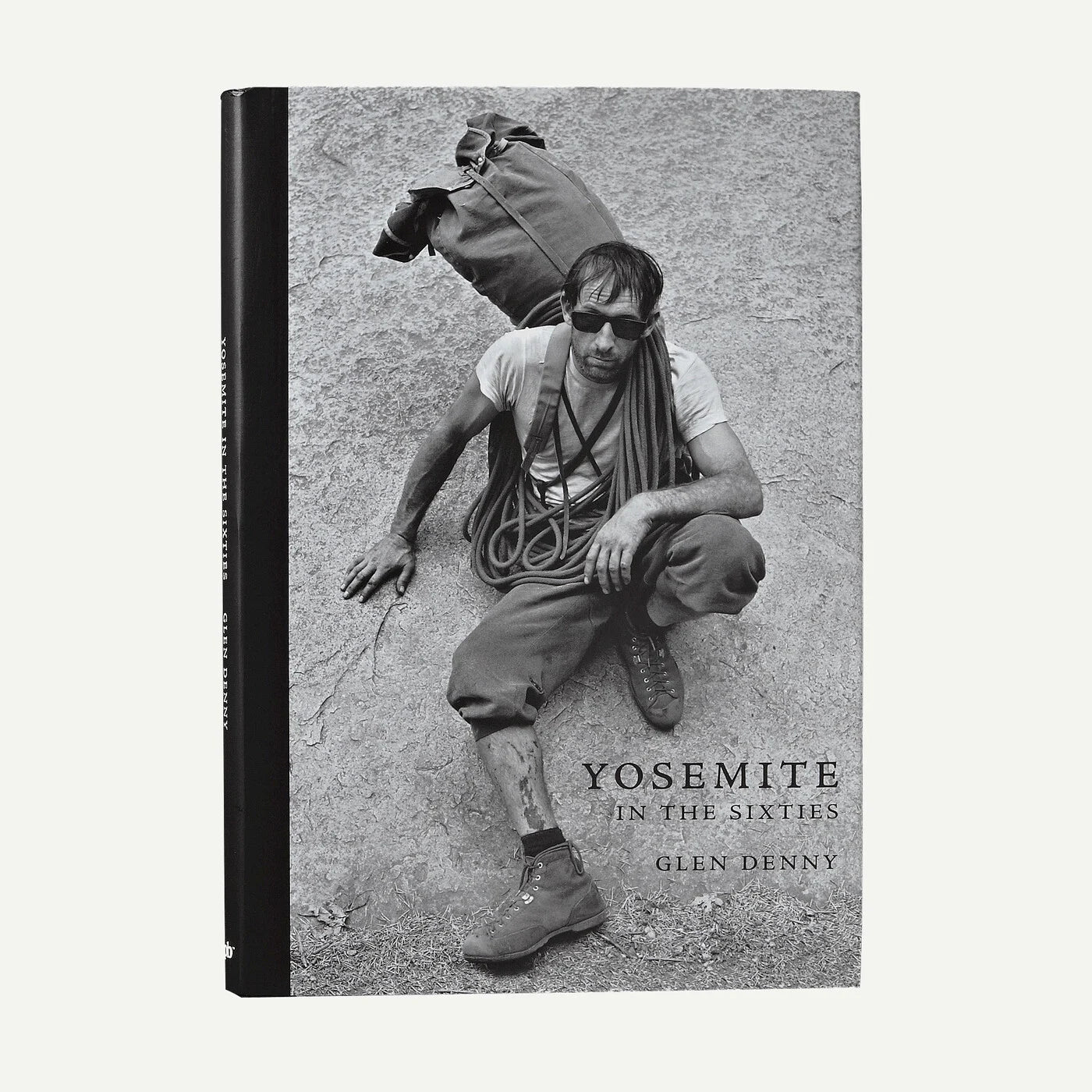 A hardcover book titled "Yosemite in the Sixties" by Glen Denny, featuring a black-and-white cover photograph of a man climbing in Yosemite with a backpack and rope. The book is photographed upright against a plain light background.