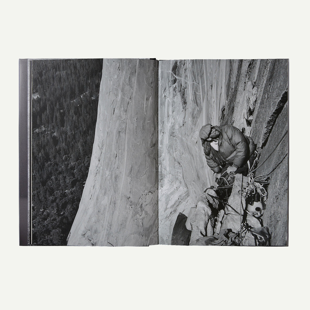 An open book or photo album showing two black-and-white photographic pages: one of a large rock face and forest below, and one of a climber on a steep cliff with ropes and gear.