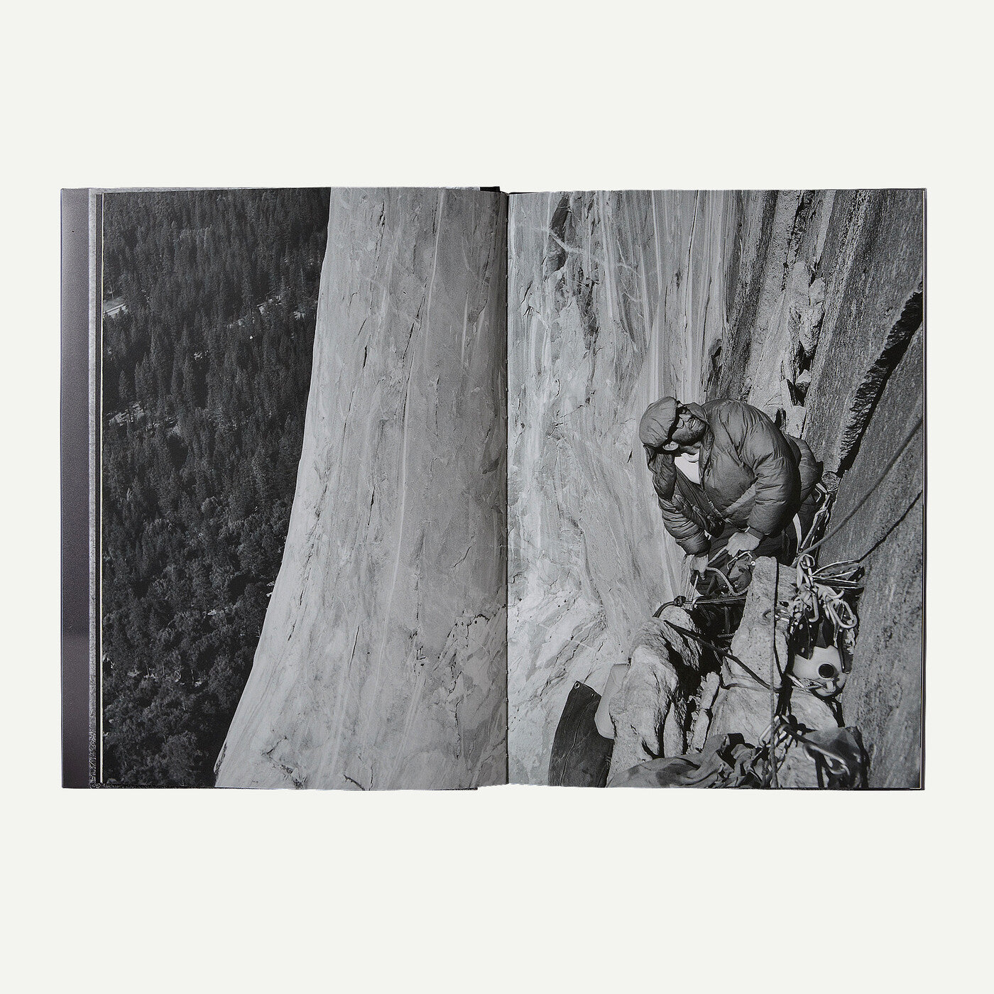 An open book or photo album showing two black-and-white photographic pages: one of a large rock face and forest below, and one of a climber on a steep cliff with ropes and gear.