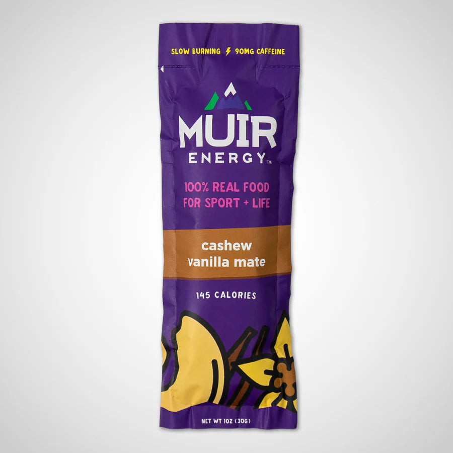 A single Muir Energy cashew vanilla mate stick pack on a light gray background. The packaging is primarily purple with a brown band in the middle, white and pink text, and yellow illustrations of cashews and vanilla beans at the bottom.