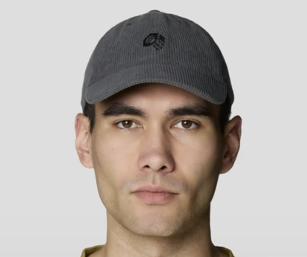 A man wearing a dark gray corduroy baseball cap with a small black embroidered logo on the front, photographed against a light gray background.