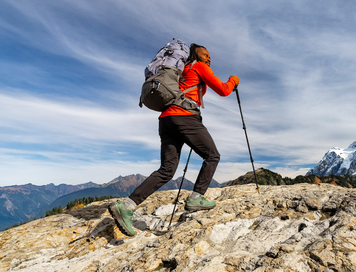a person hikes over some rocks with mt. shuksan in the background