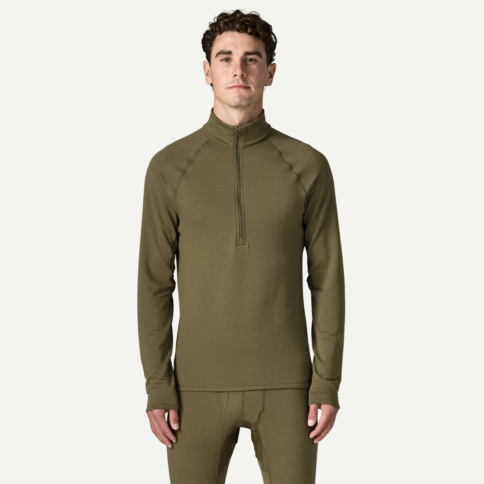 A man modeling a matching olive green long-sleeve quarter-zip performance top and matching pants against a light off-white background.