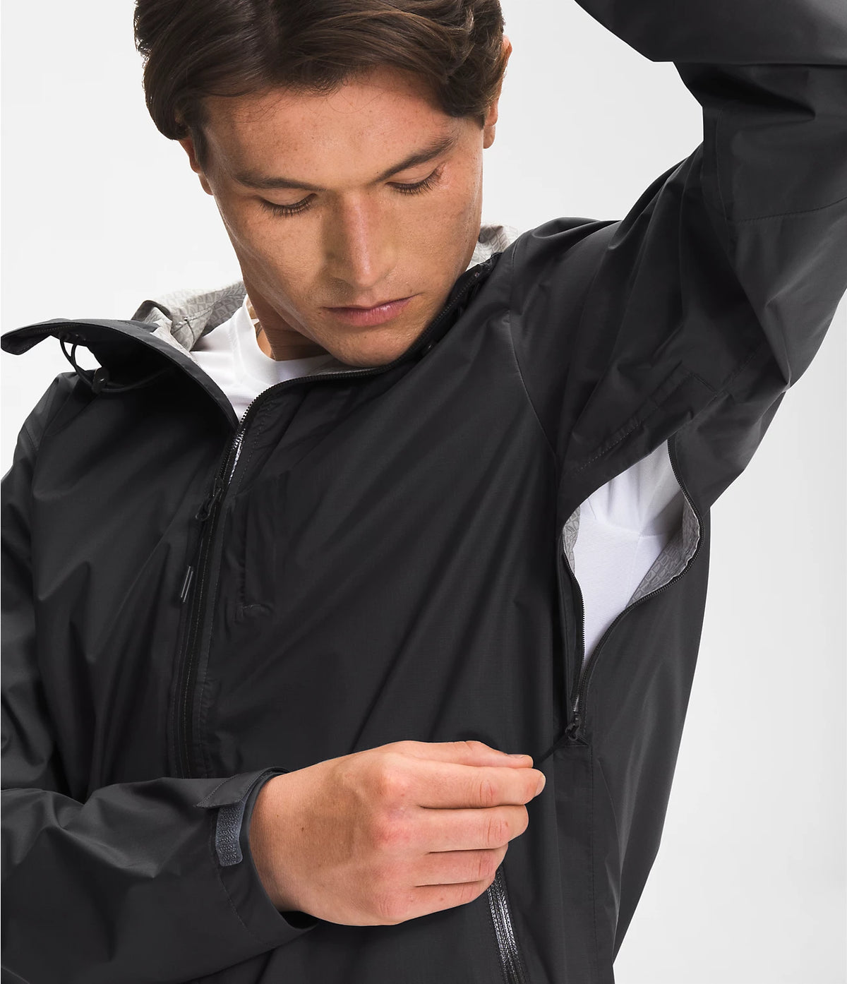 A man wearing a black lightweight zip-up jacket over a white shirt, shown in a close-up studio shot against a light gray background.