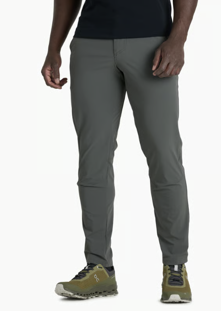 A person wearing slim-fit gray pants and olive green trail running shoes, cropped from the chest down against a plain white studio background.
