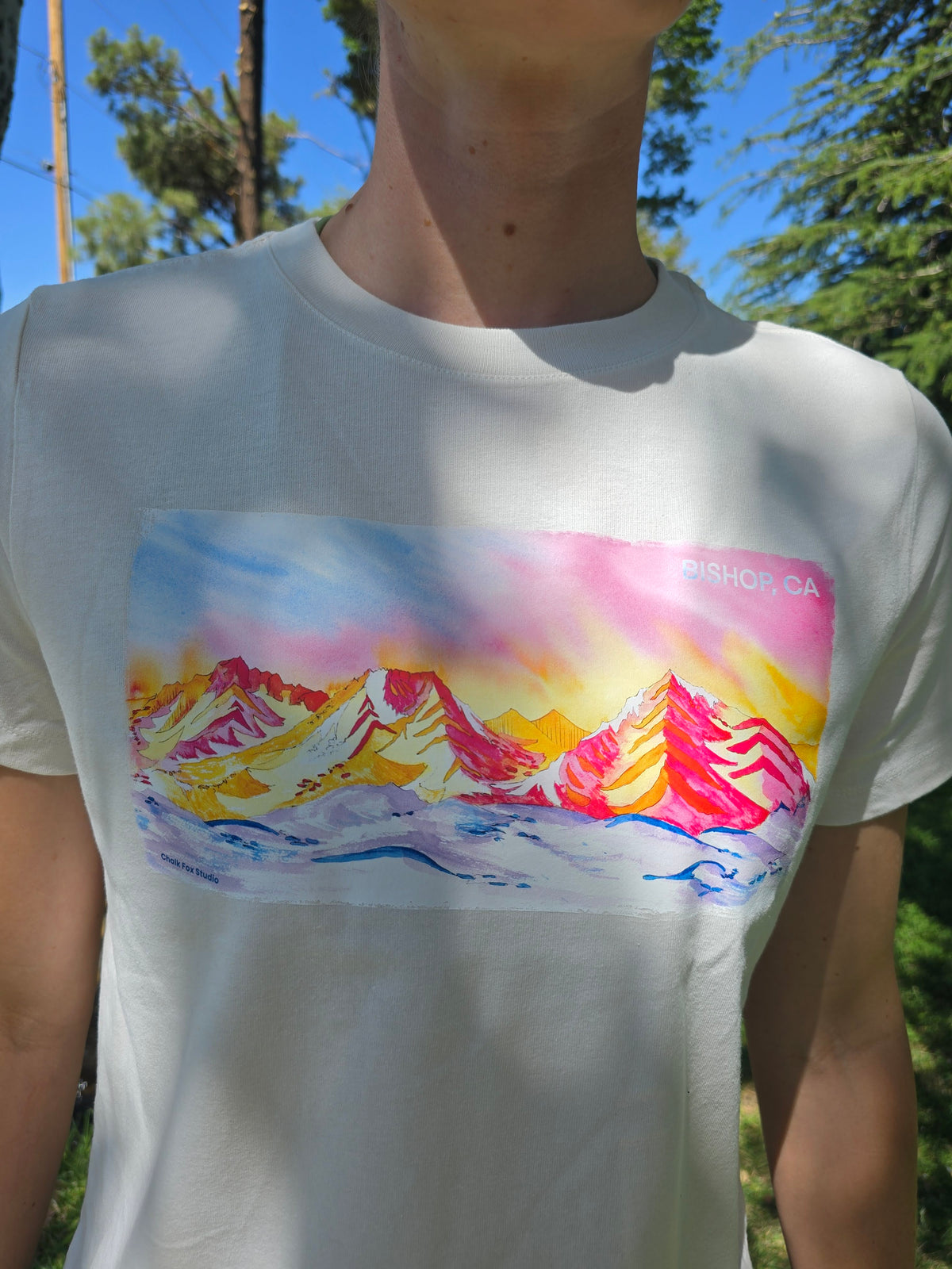 white women's t-shirt with colorful mountain graphic, worn by a person