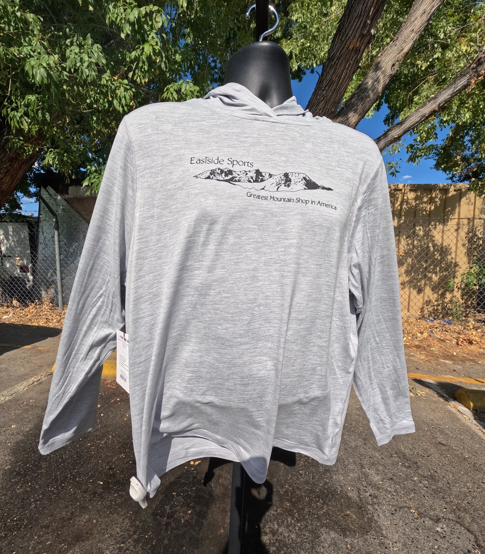 A light heather gray long-sleeve hooded shirt displayed on a black mannequin outdoors. The front has a black mountain graphic with the text 'Eastside Sports' and 'Greatest Mountain Shop in America.