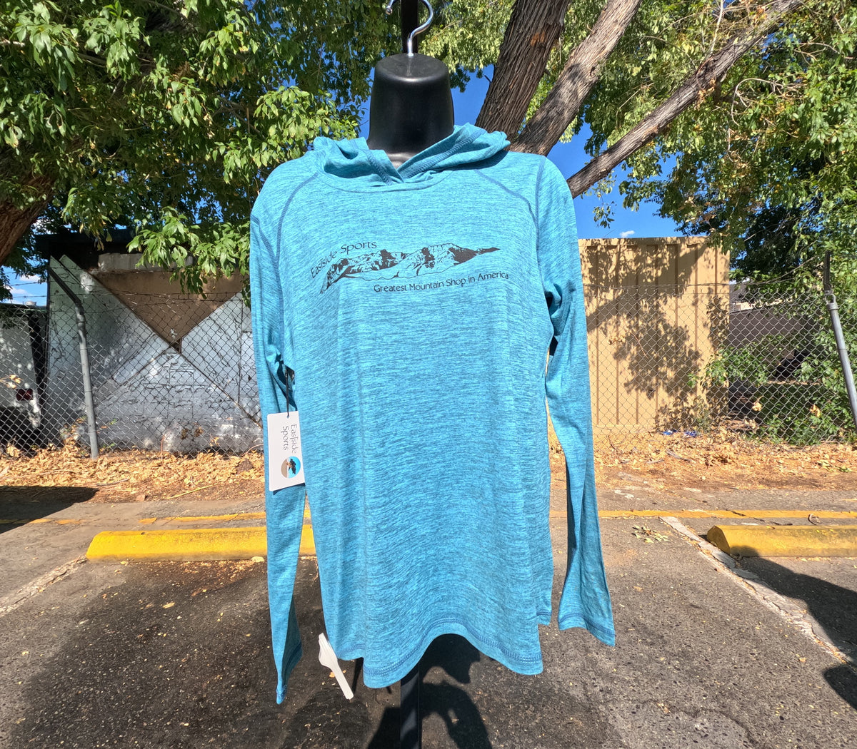 A bright blue heathered long-sleeve hooded shirt displayed on a black mannequin outdoors. The shirt features a black graphic of three mountains with the text 'Eastside Sports' and 'Greatest Mountain Shop in America' printed on the chest.