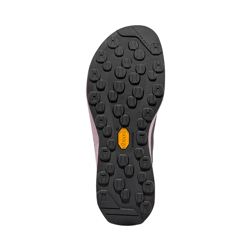 The black rubber outsole of a shoe, showing a pattern of circular lugs and a yellow Vibram logo, photographed from a top-down view on a white background.