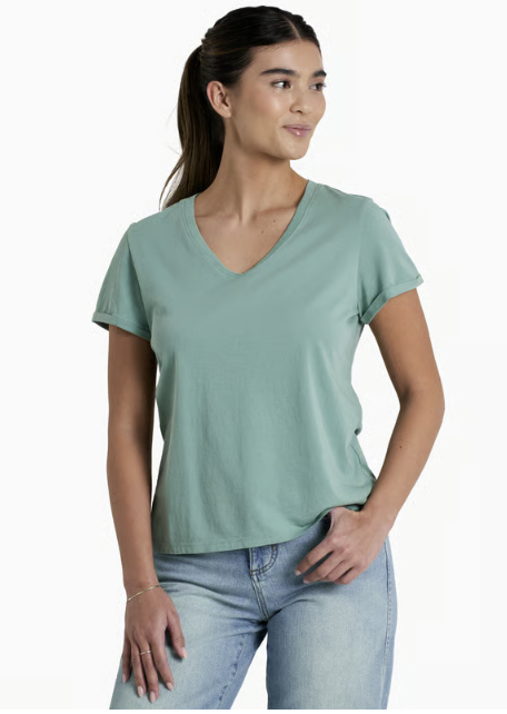 A woman wearing a sage green V-neck short-sleeve t-shirt and light wash blue jeans, standing against a plain white studio background.