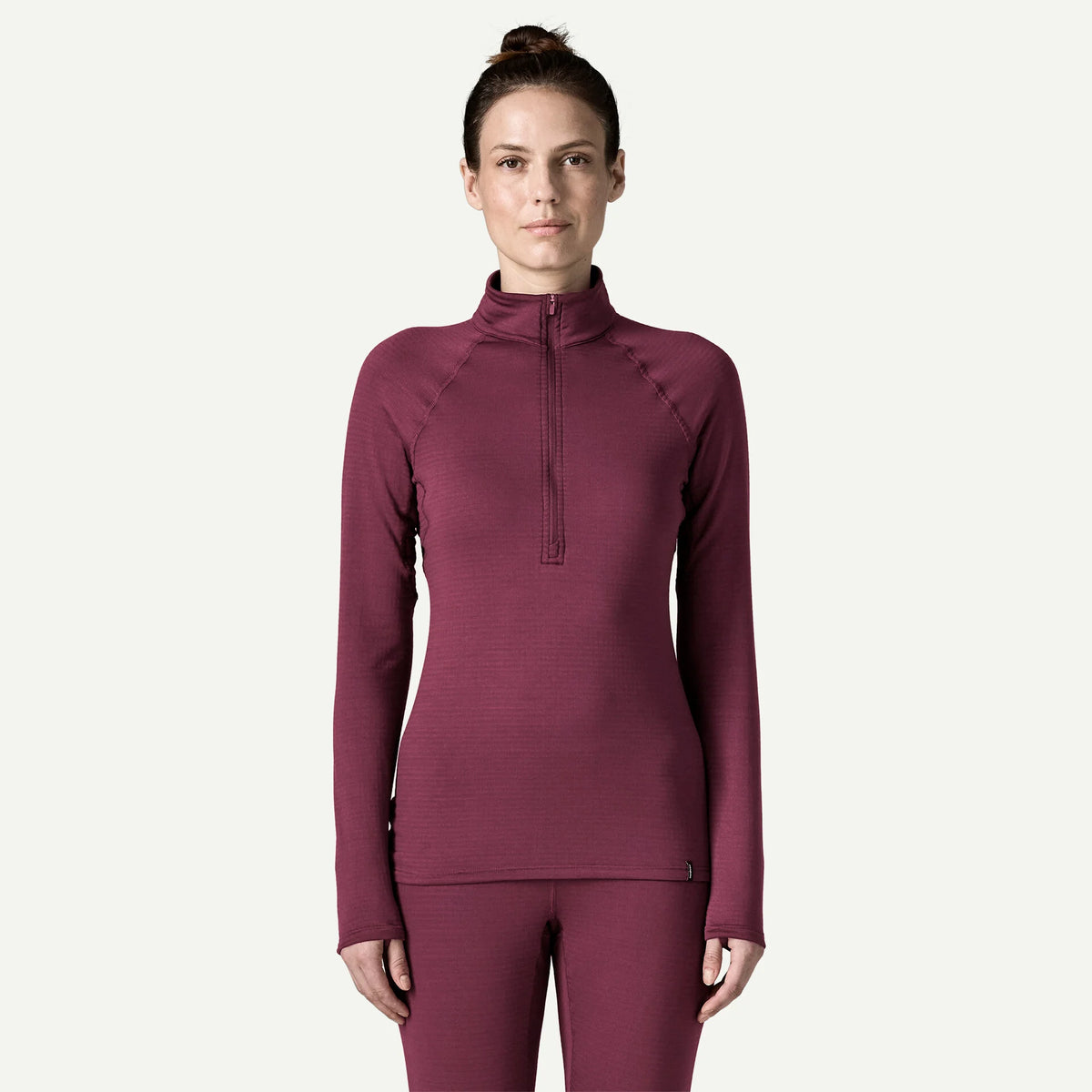 A woman modeling a ribbed long-sleeve quarter-zip athletic top in a deep berry/plum color, paired with matching leggings, against a clean off-white background.