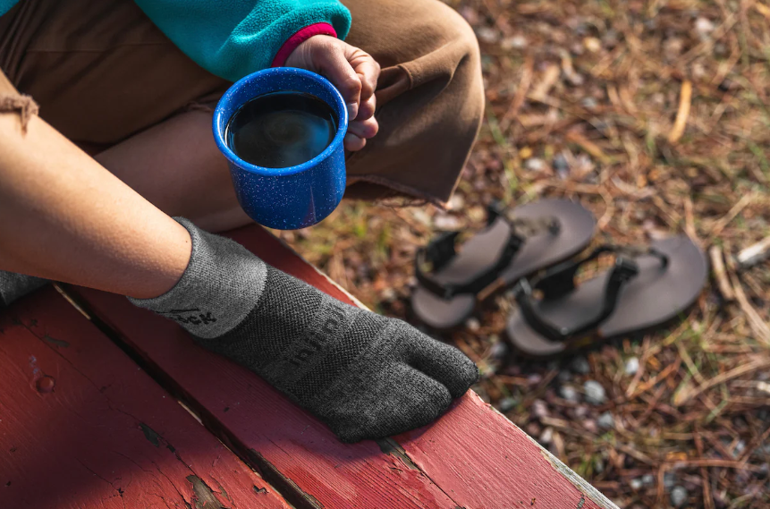 injinji bedrock split toe sock on a foot on a bench plus coffee