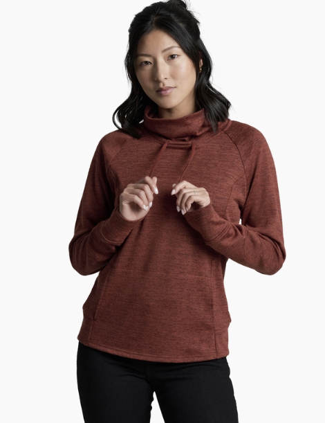 A woman wearing a heathered rust-brown mock neck athletic top and black pants, standing against a plain white studio background.