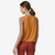 the patagonia womens capilene cool trail cropped tank top in the color golden caramel, back view on a model